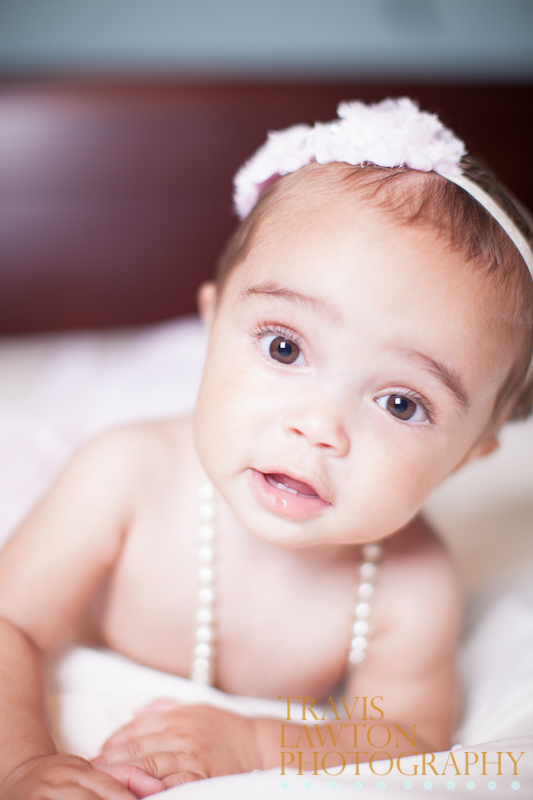 Beautiful baby laying on a bed staring into the camera smiling